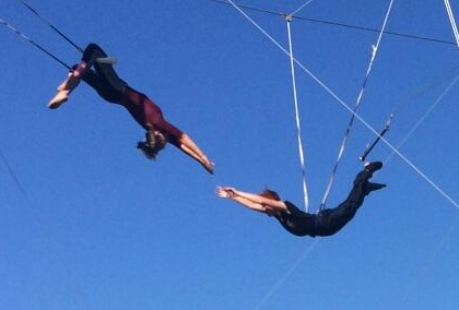 Aerialist upside down on flying trapeze against blue sky