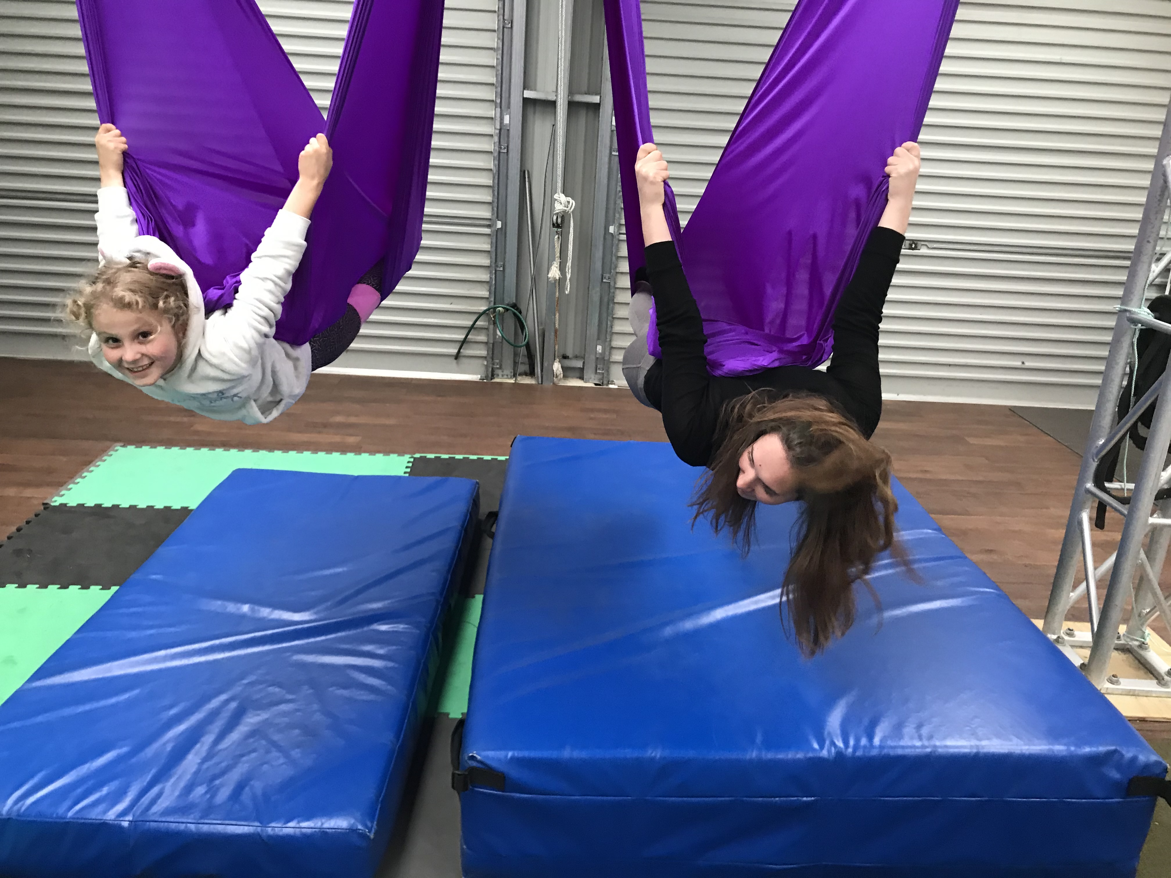 Two girls hanging upside down on silks smiling